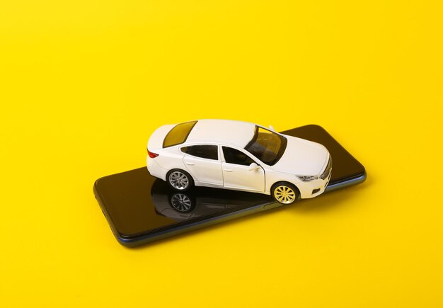 写真 黄色い背景のスマートフォンを搭載したおもちゃ車モデル