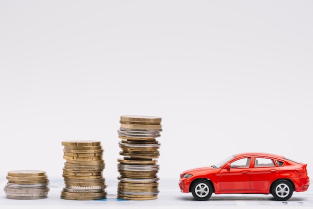 Toy car near the increasing stack of coins against white background