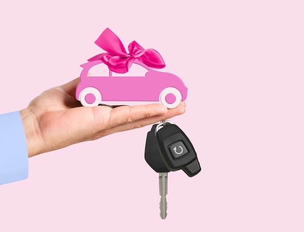 Toy Car with bow and key on dealers hand on a pink background. Car purchase concept