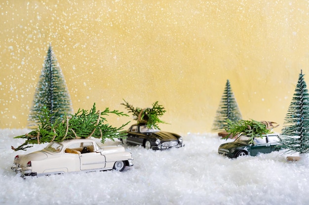 Toy cars in the forest among the snowdrifts that are delivers Christmas trees. Blurred background. Magic atmosphere, concept of Christmas holidays. Greeting card.