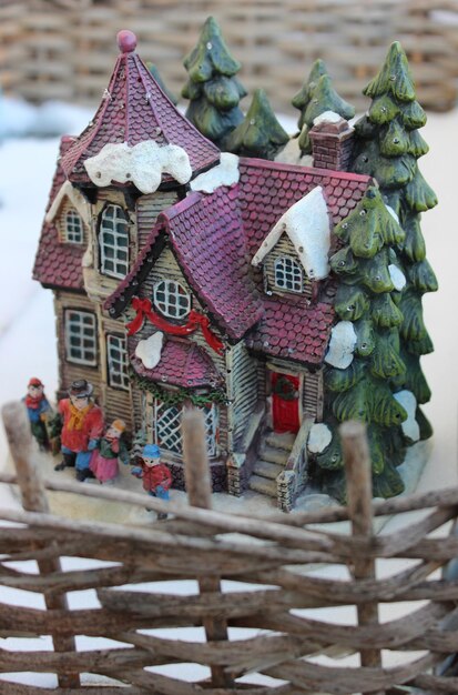 Photo a toy diorama of small house in a winter setting surrounded by a wattle fence