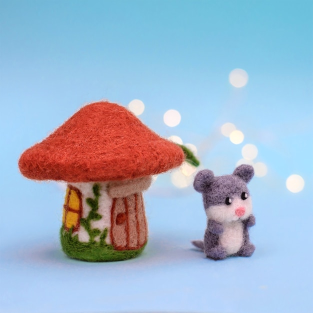 Toy felt house mushroom with a door and windows and a cute little gray mouse on a light blue background with bokeh