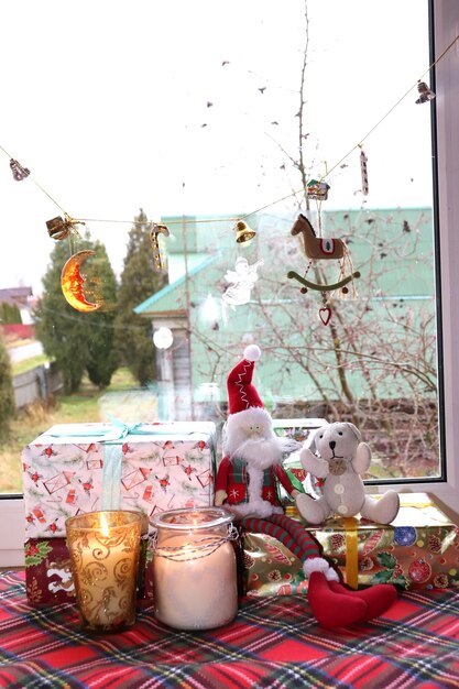 Игрушечный гном с плюшевым медведем сидит на рождественских подарках с свечами возле окна