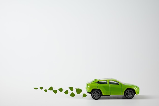 A toy green car rides over the background with an exhaust from birch leaves. The concept of reducing CO2 emissions from vehicles