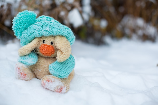 игрушечный заяц в шапке и шарфе сидит на снегу
