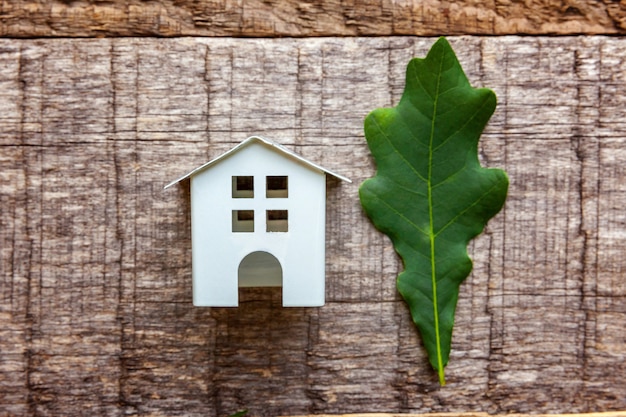 Toy House and green oak leaf on wooden background