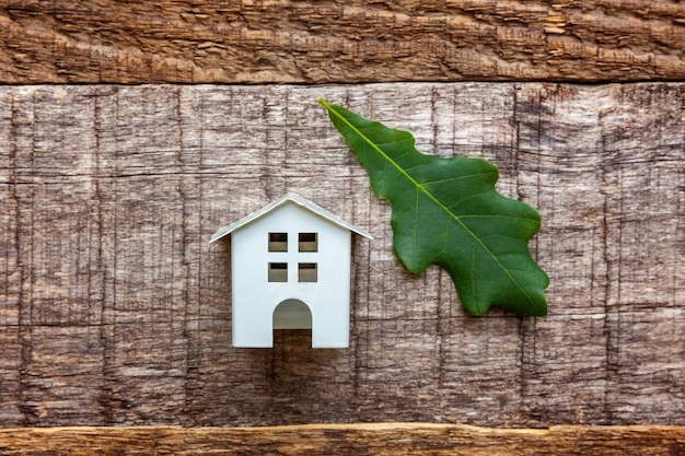 Toy House and green oak leaf on wooden background