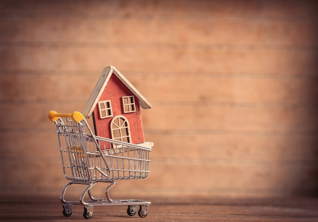 Toy house in a little shopping cart on wooden table