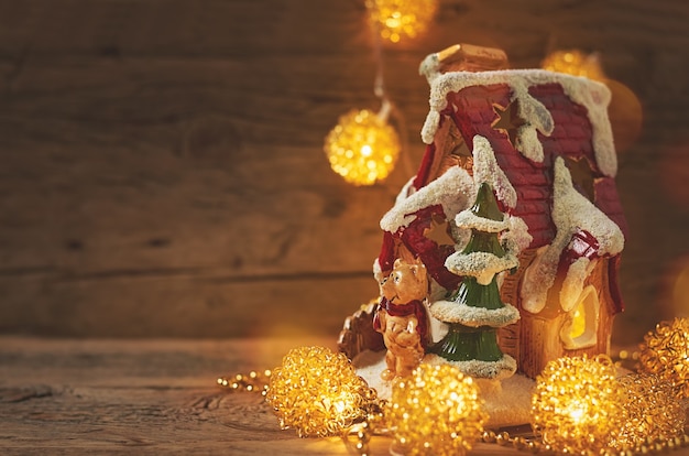 Foto casa giocattolo con un orsacchiotto e luci di natale su uno sfondo di legno