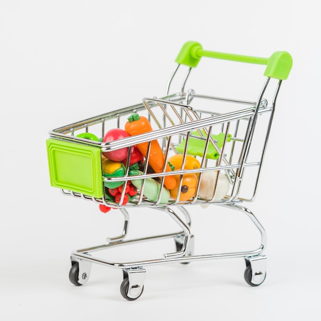 Toy miniature shopping trolley with an assortment of colorful oversized fruits and vegetables