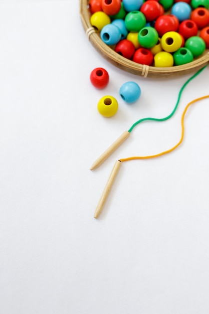 Toy for motor skills development close up of colorful wooden beads lace and needle over white background