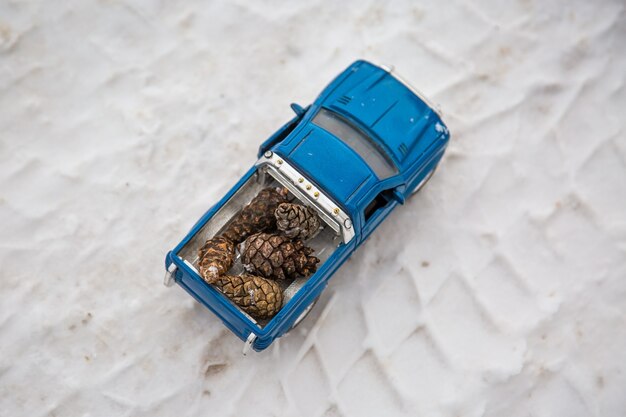 Camioncino giocattolo su strada invernale trasportare pigne sulle tracce di pneumatici di un'auto reale sulla neve