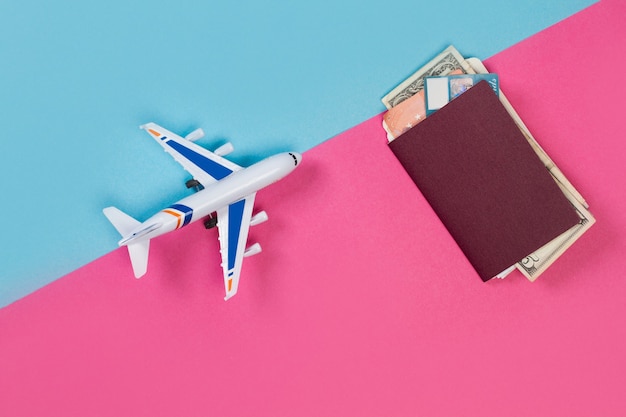 A toy plane a passport and a boarding pass on a pink and light blue  background