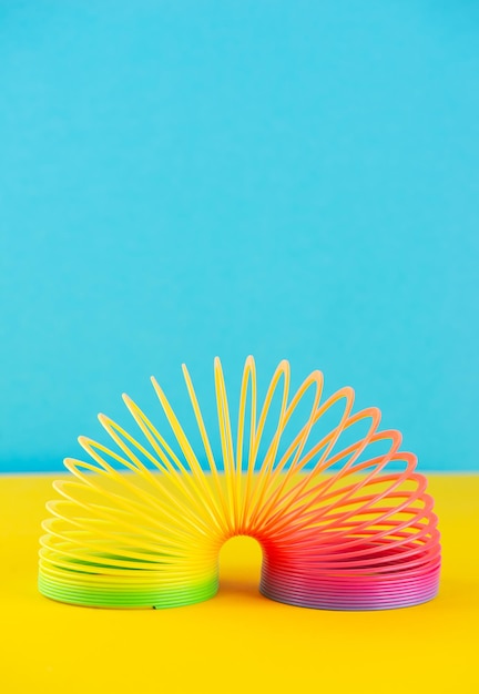 Игрушечная пластиковая красочная радужная спираль для игры на синем-желтом фоне Вертикальная ориентация