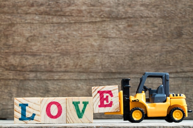 Toy plastic forklift hold block E to compose and fulfill wording love on wood background