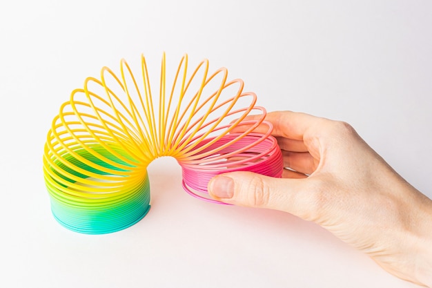 Игрушка пластиковая радуга в руках на светлом фоне.