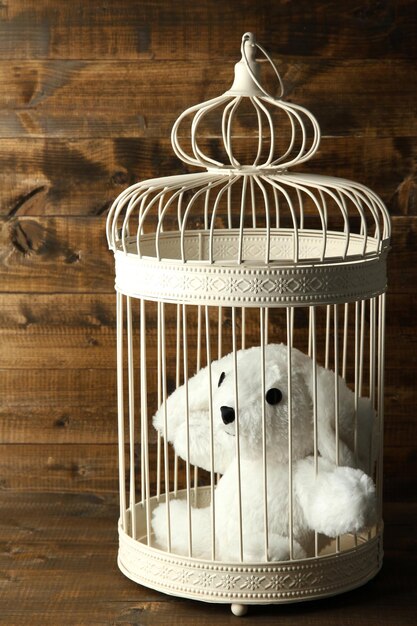 Toy rabbit in decorative cage on wooden background