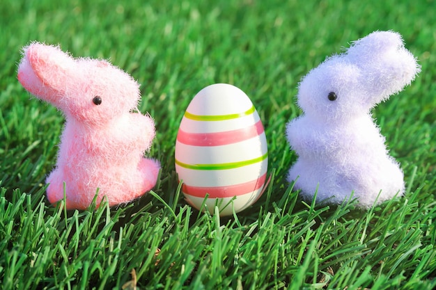 Toy rabbits with Easter egg on green grass