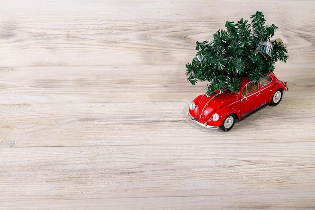 Toy red car with a Christmas tree on a wooden background place for text