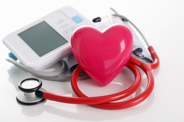 Toy red heart lying near electronic tonometer and stethoscope closeup cardiological medical
