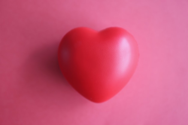 Toy rubber heart lying on red background closeup top view