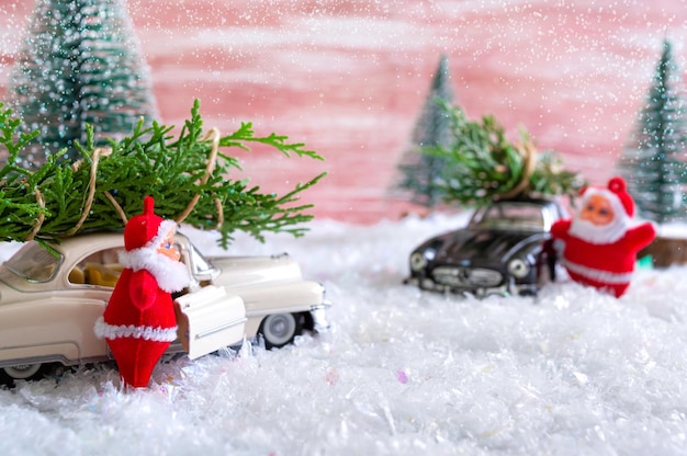 Toy Santa in the forest among the snowdrifts waves to cars that are delivers Christmas trees