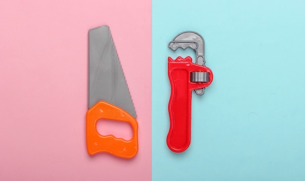 Toy saw and adjustable spanner on a blue-pink pastel background. Top view