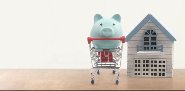 Toy shopping cart and Piggy bank. Consumer society trend and Model house