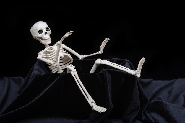 A toy skeleton crawling out of the grave and waving greeting on\
a black background halloween greeting card