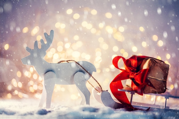 Photo toy sleigh with a christmas gift pulled by a wooden reindeer in snow