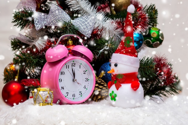 A toy snowman near the clock, which shows the approach of 12 hours, the new year. A snowman, a clock near a Christmas tree, goes snow_