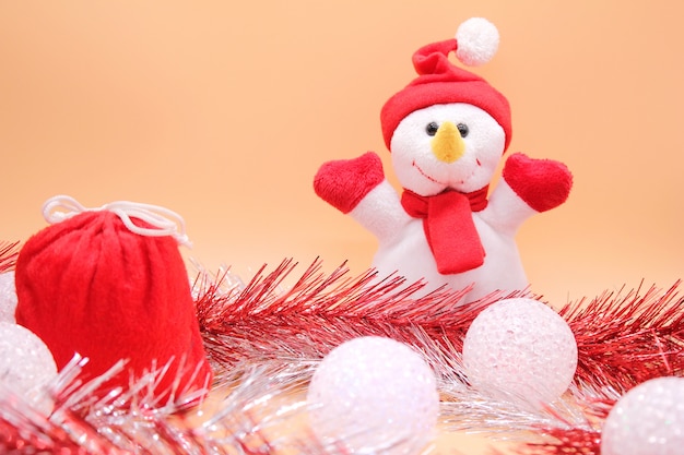 Toy snowman and a red bag with gifts among tinsel and Christmas balls.