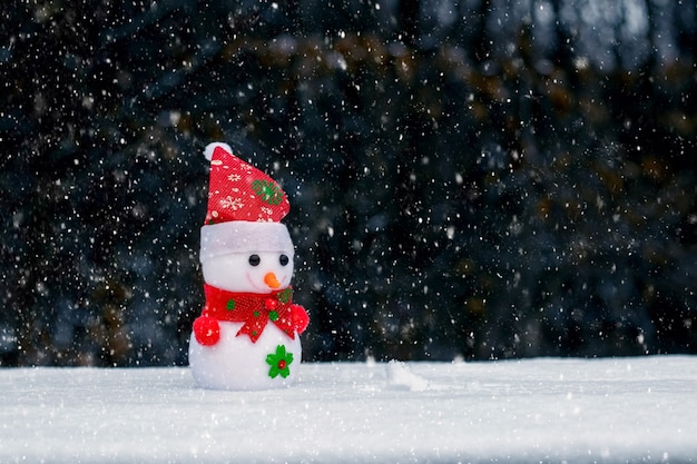 Toy snowman in the woods on a dark background during a snowfall