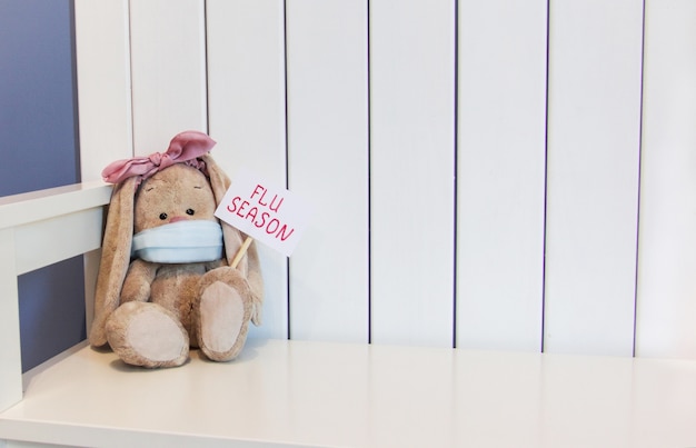 Photo toy soft rabbit sits in a mask and holds a sign flu season