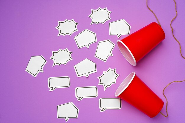 Toy telephone made of plastic cups and string with speech bubbles on purple surface