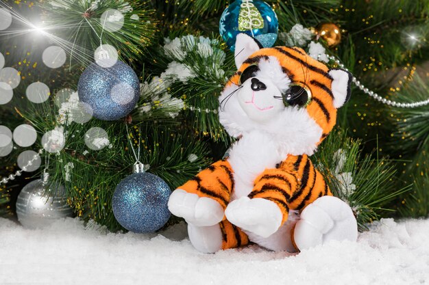 Toy tiger cub sitting near a Christmas tree in the snow