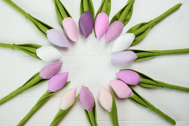 Toy tulips laid out in a circle on a white wooden background.