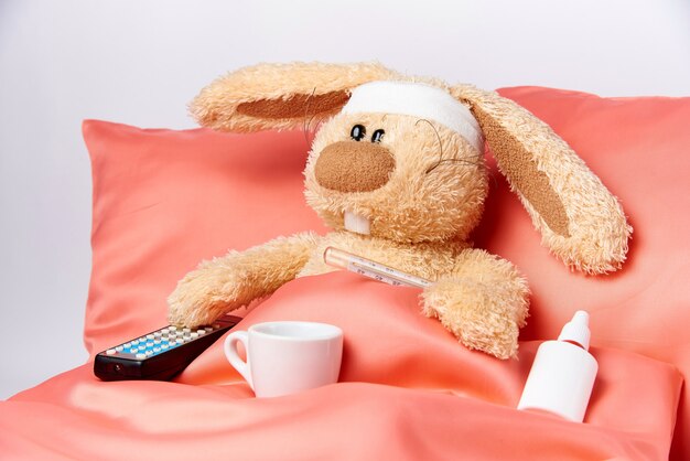 A toy unhealthy rabbit with mediciner and a TV remote control in bed.