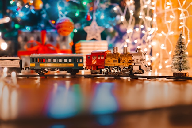 Toy vintage steam locomotive on the floor under a decorated Christmas,  bokeh lights garland.