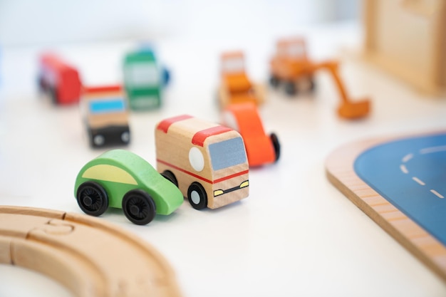 a toy of wooden school bus drives beside a green car with many kinds of car behind it of a vehicle toy set for children in an indoor playground