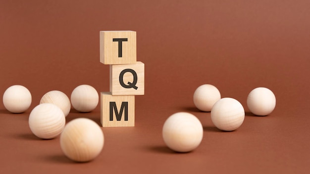 TQM word is written on wooden cubes on a brown background closeup of wooden elements