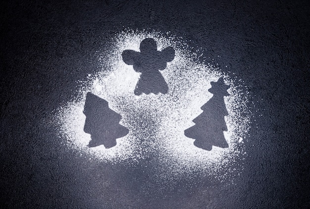 Traces from a stencil in the form of a Christmas tree and angel with snowflakes from flour on black