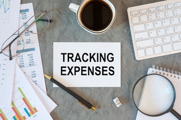 Tracking Expenses is written in a document on the office desk with office accessories, keyboard and diagram