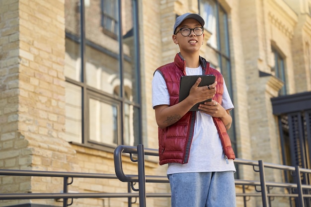 Отслеживание заказа. Молодой азиатский курьер использует приложение на цифровом планшете, стоя на улице. Концепция службы доставки