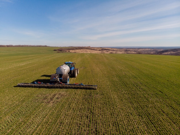 Trattore che applica fertilizzanti minerali liquidi al suolo sul frumento autunnale