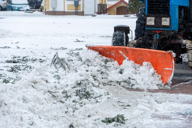 A tractor cleans snow in the city in winter after a snowfall Cleaning city streets from snow Tractor driver at work in the city square during a snowstorm