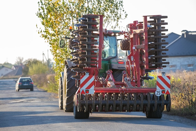 Tractor combine with disc harrows driving along rural road on sunny day.