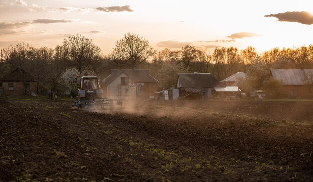 The tractor cultivates the land in the field at sunset Dust Industry agriculture