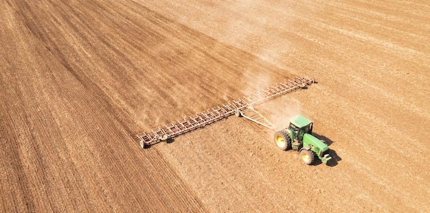 A tractor in the field cultivates the soil before the start of the sowing campaign Drone view