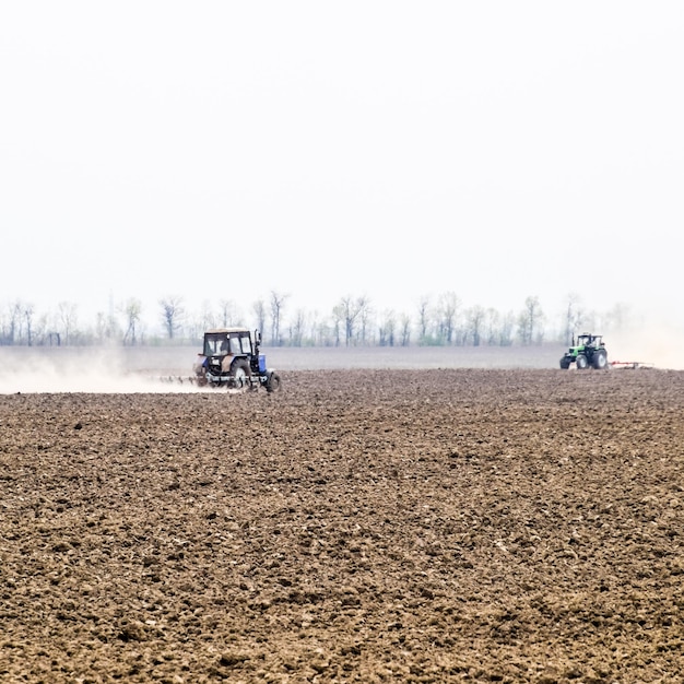 The tractor harrows the soil on the field and creates a cloud of